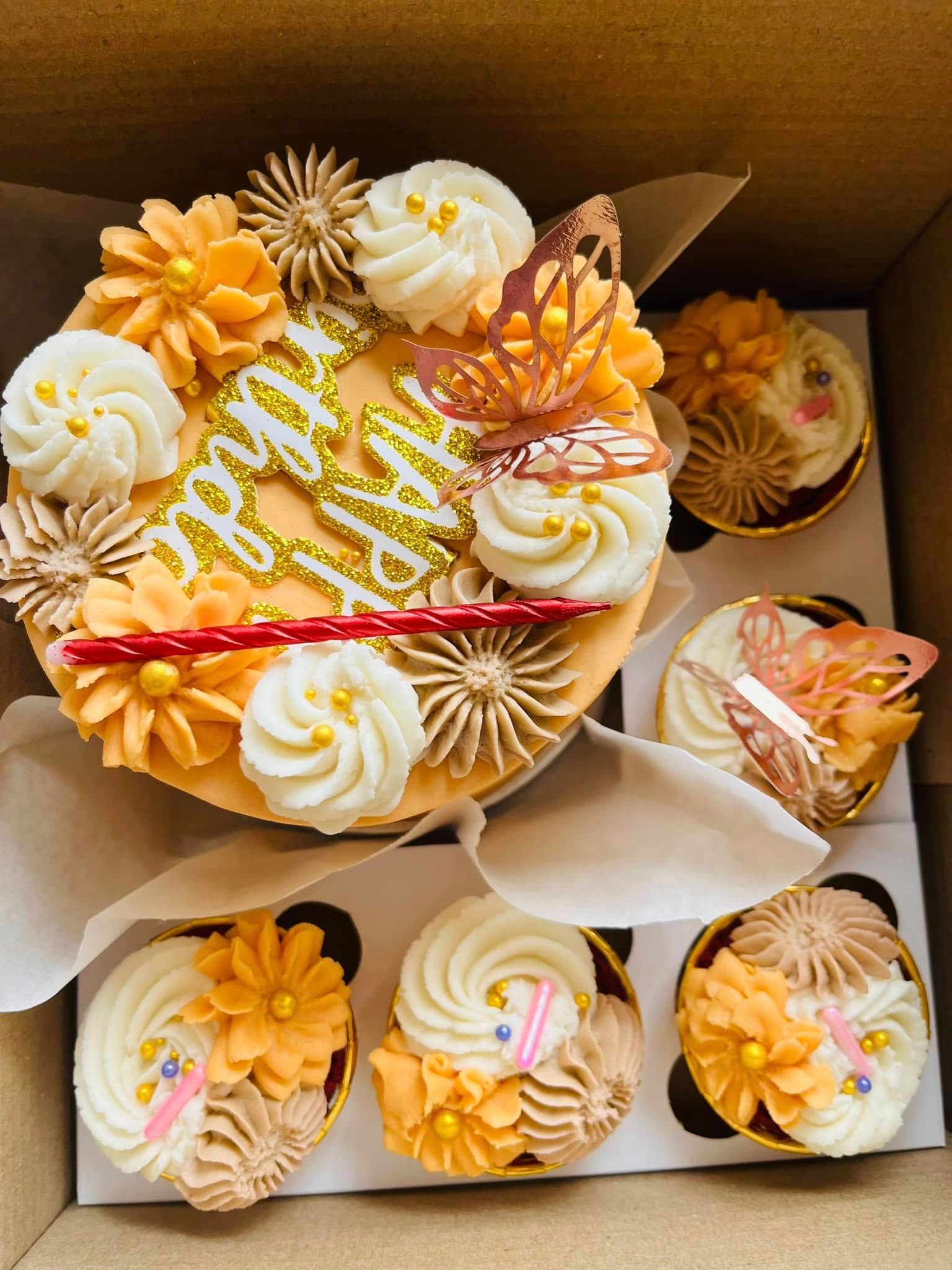 A marigold buttercream cake piped with orange and cream flowers, boxed with matching cupcakes
